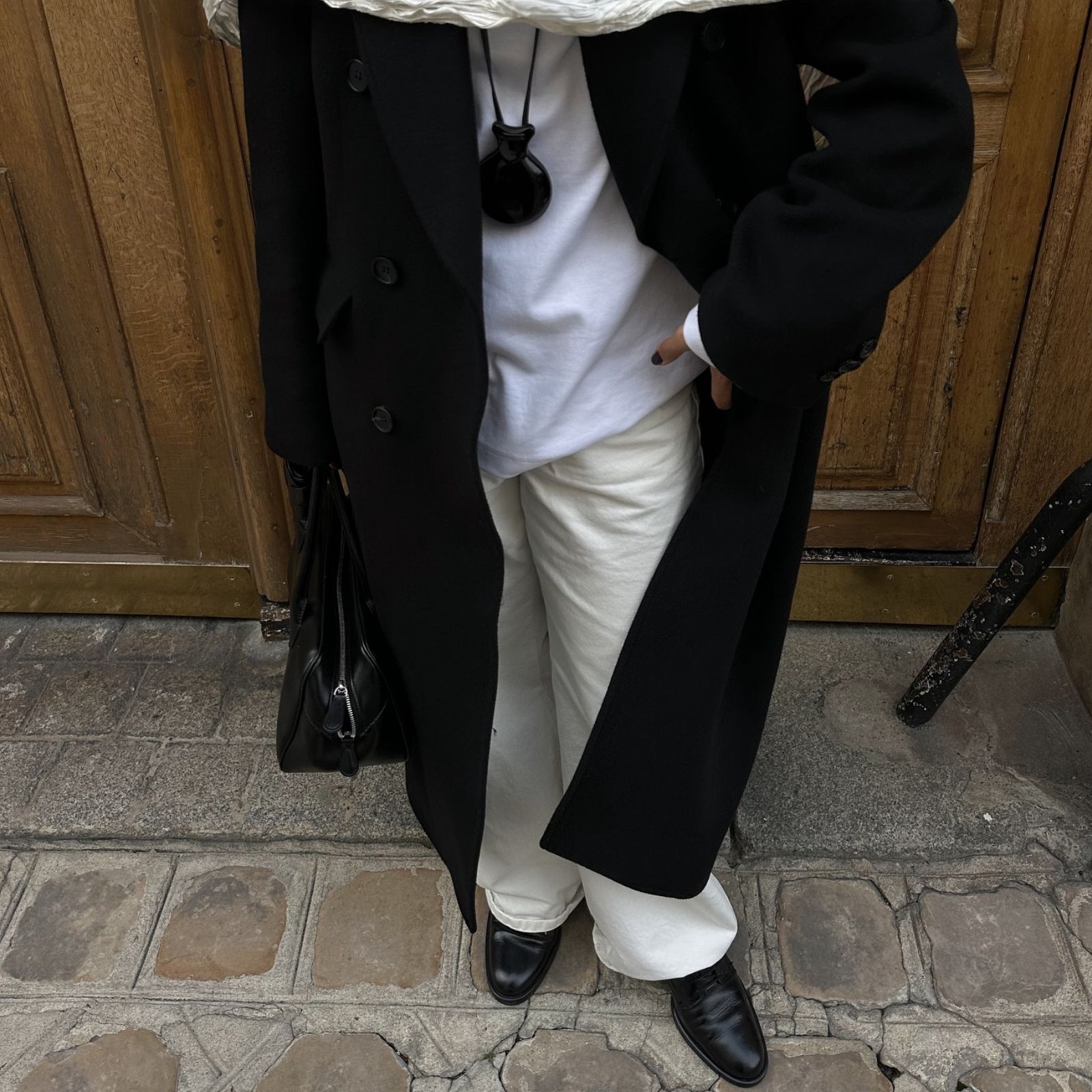 A woman wears smooth leather loafers with white pants and a black overcoat