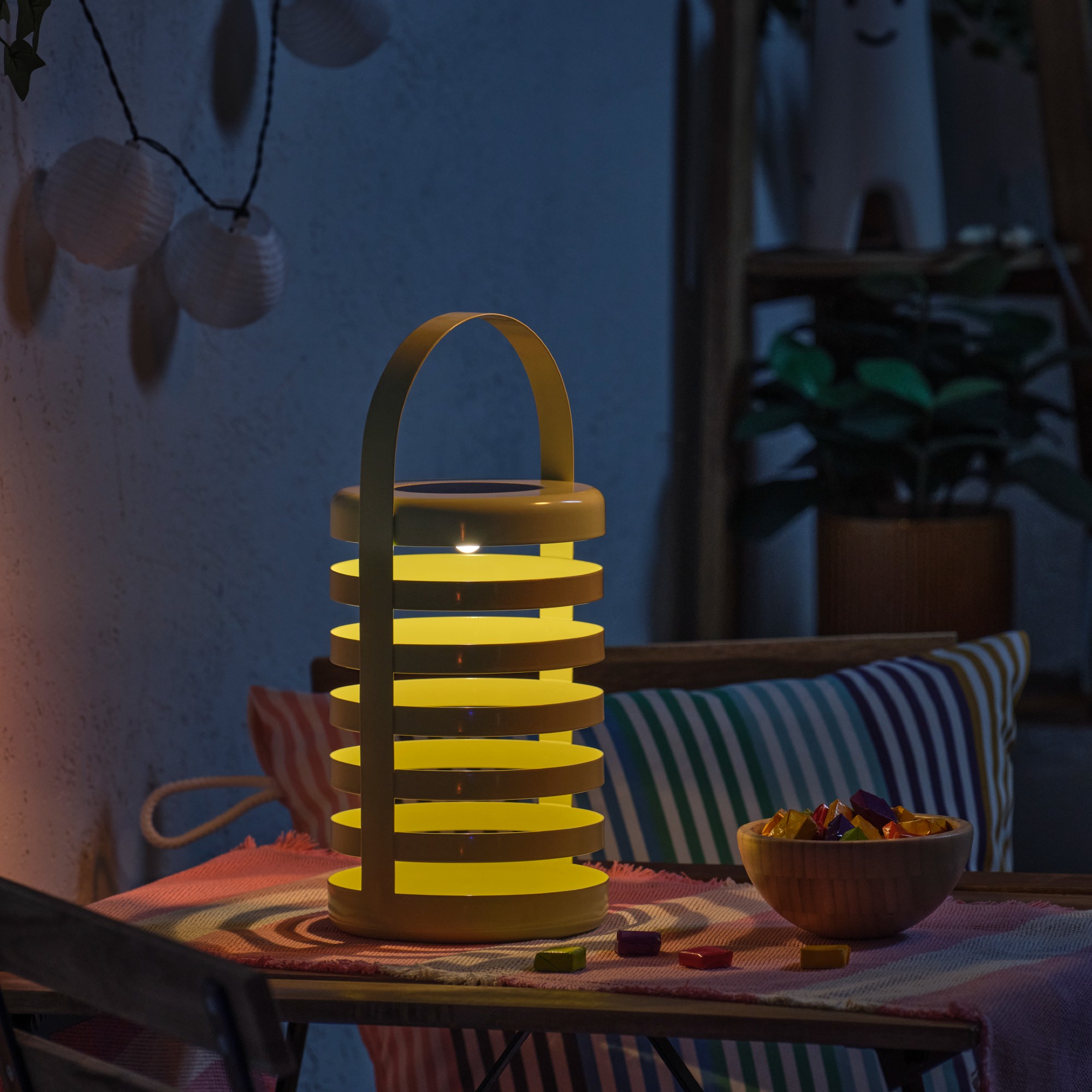 IKEA's SOLVINDEN solar outdoor lantern on a garden dining table lit up in the dark