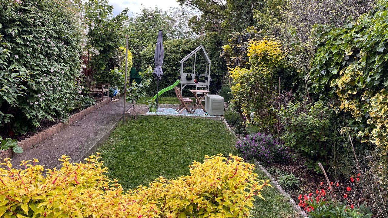 A photo of a long and narrow back garden with a concrete path running down one side