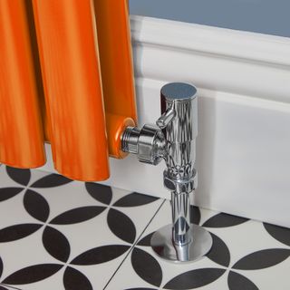Orange radiator with silver valve on black and white floor