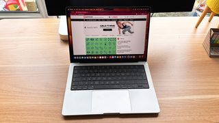 A MacBook Pro 14-inch open on wooden desk with Creative Bloq on screen