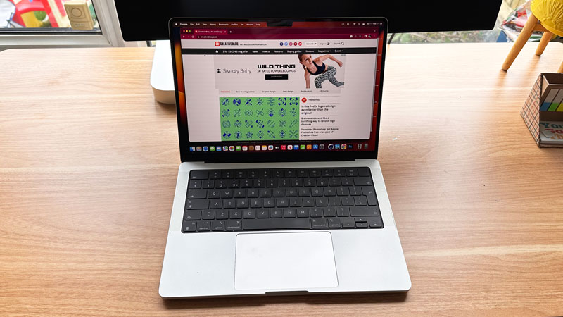 MacBook Pro 14-inch open on wooden desk with Creative Bloq on screen