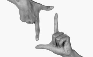 Grey toned photograph of two hands making the 'hand frame' symbol