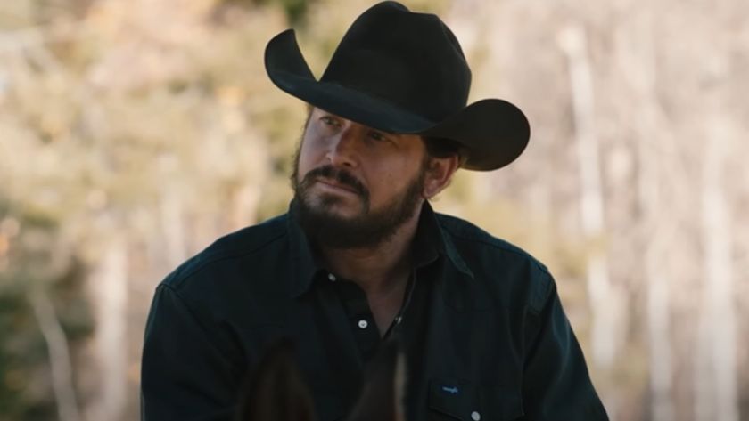 Cole Hauser as Rip Wheeler sitting outside looking up and to his left while wearing a black cowboy hat. 