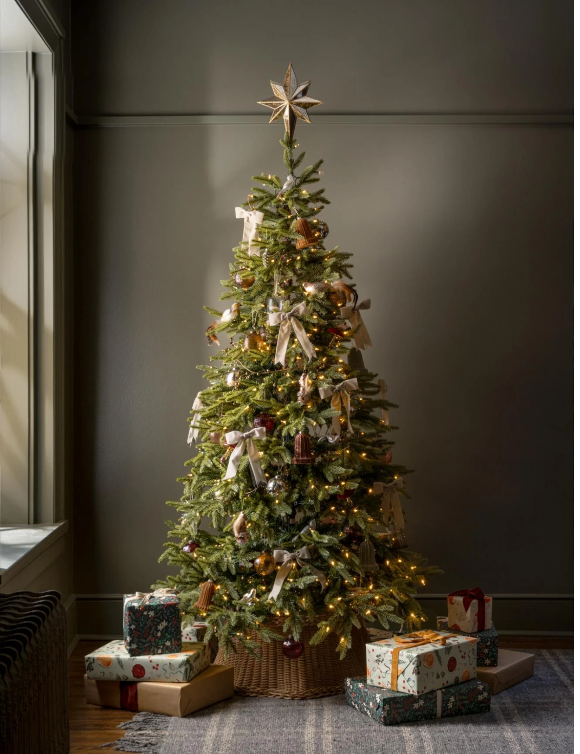 Classically decorated Christmas tree featuring a scalloped wicker tree skirt, bow ornaments, and a golden tree-top star