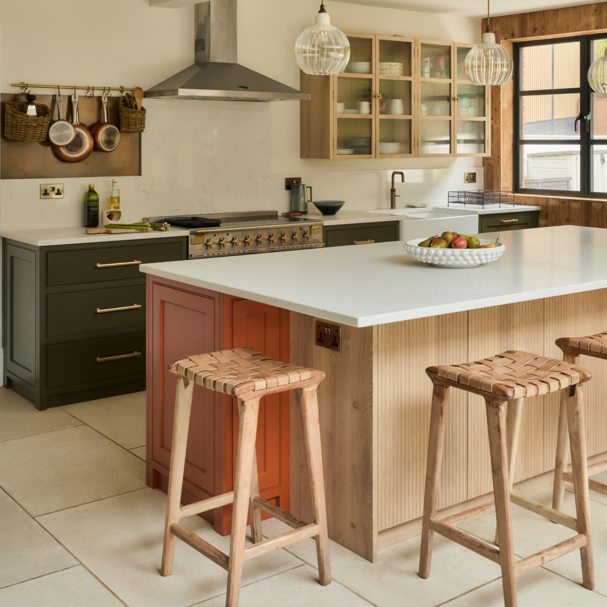 rustic kitchen with terracotta and dark green cabinets, wood panelling, bar stools, hanging rail for saucepans, wall unit, white work tops