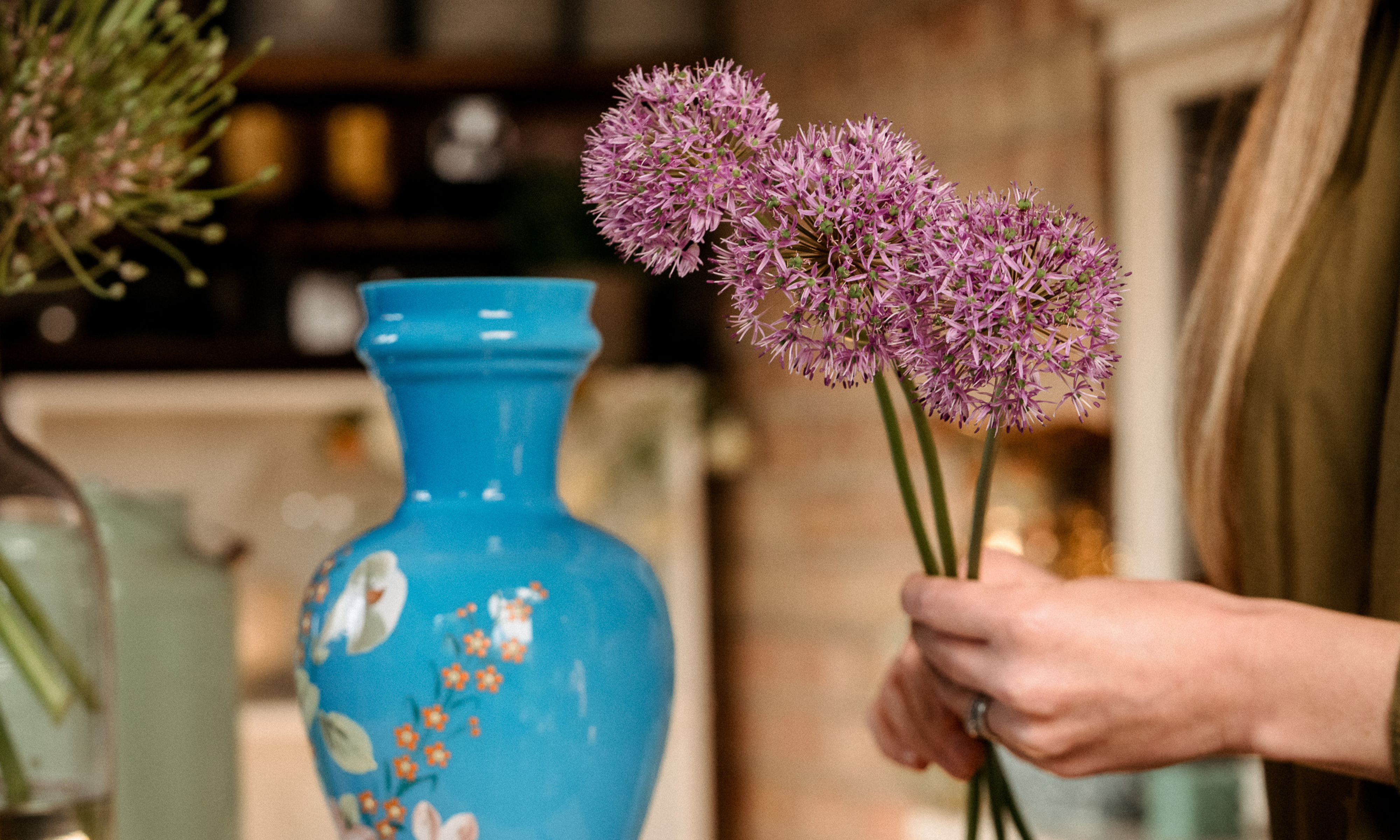 Hands holding three globe alliums next to a blue vintage vase