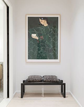 A small waiting room inside an Olympia Dumbo apartment, with a bench and a painting on the wall