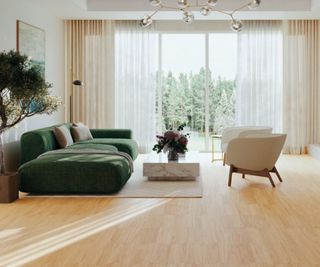 Bright living room with light wood floors, green sofa, cream chairs, marble table and large window views of trees.