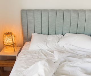 The corner of a mattress on a bed with rumpled white bedding.