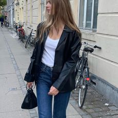 Woman wearing white t-shirt, black blazer, straight leg jeans and black bag while standing on street.