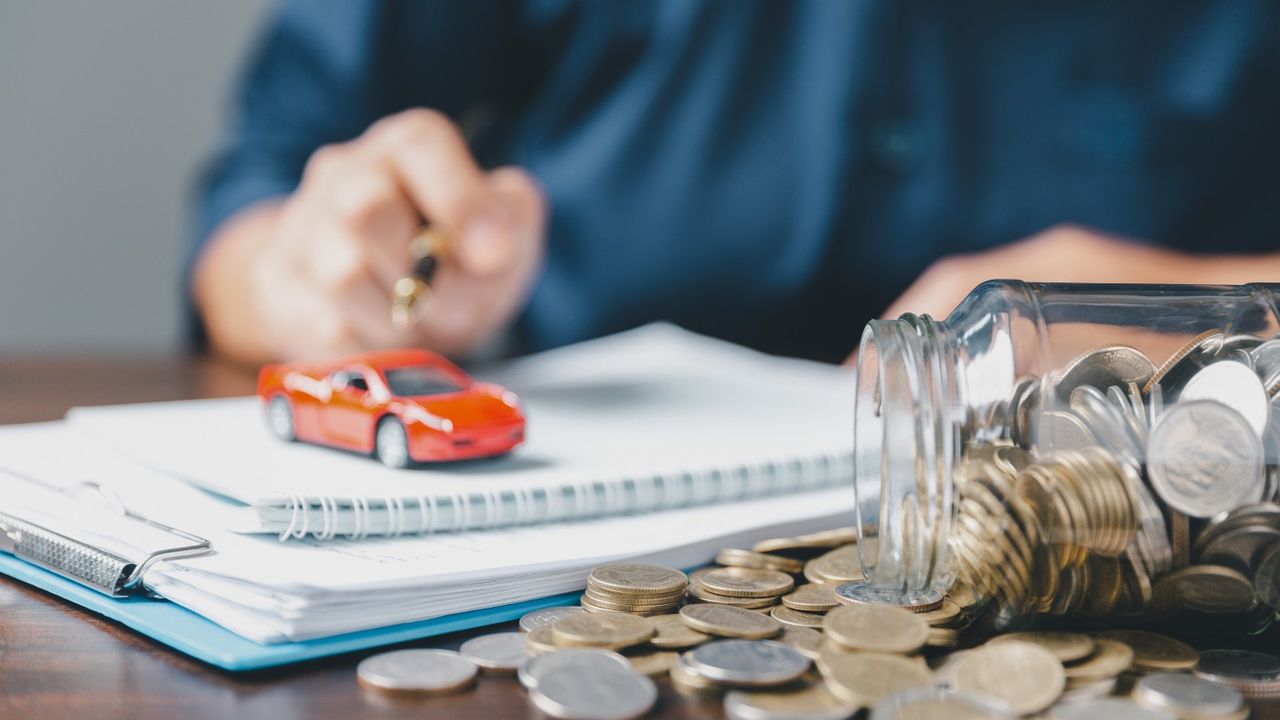 Person with hands on pad of paper with car on top and jar of money