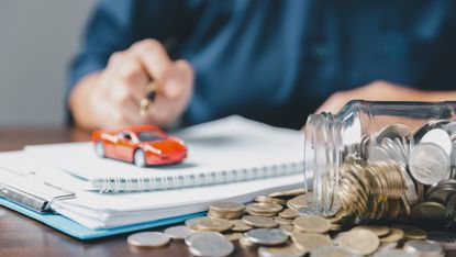 Person with hands on pad of paper with car on top and jar of money