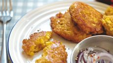 Sweetcorn fritters with onion garnish on a white plate and blue and white gingham tablecloth