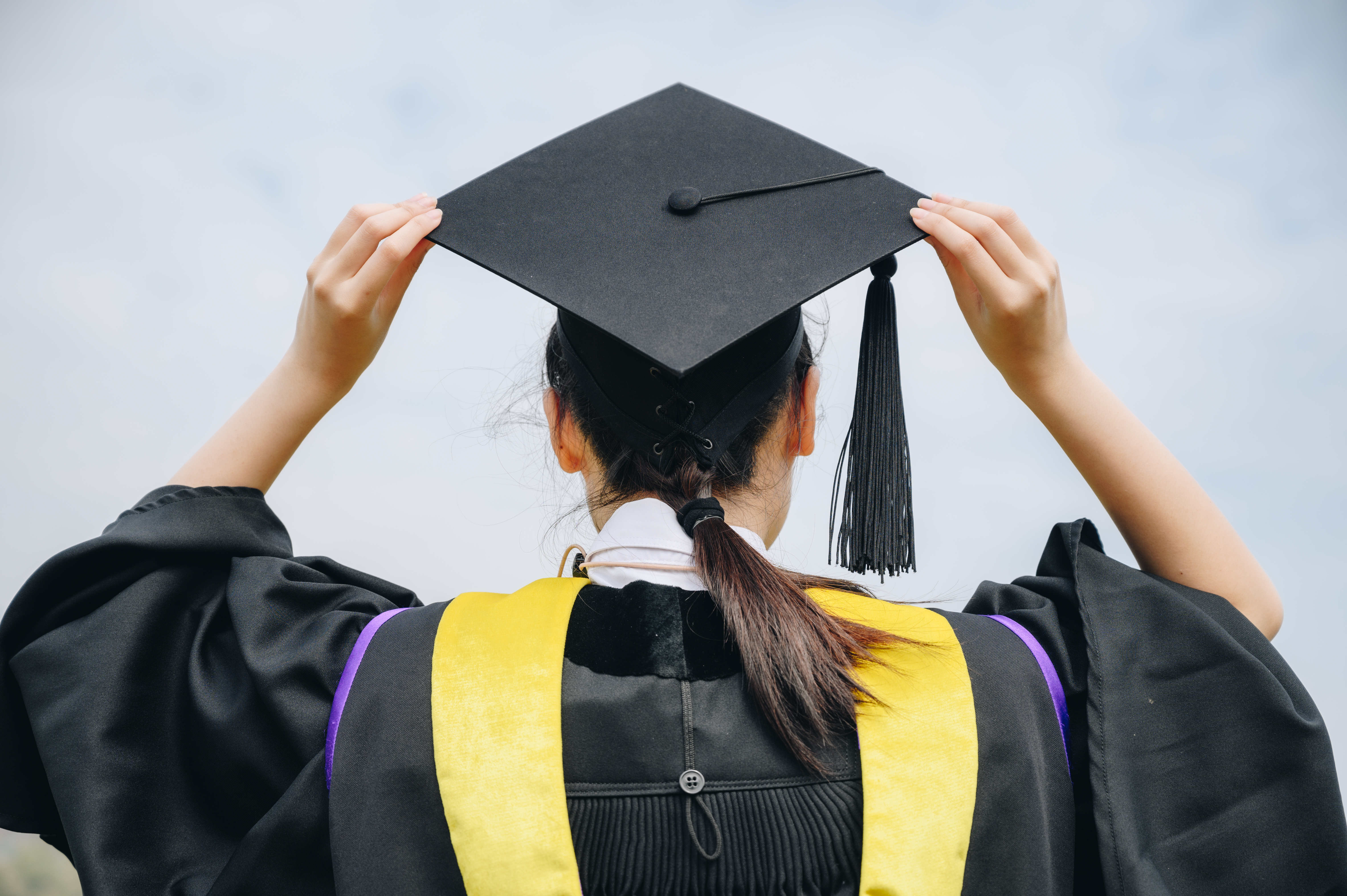 Back of student at graduation, wearing a mortarboard and gown.