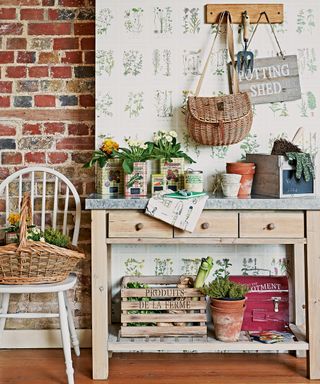 Organized potting shed ideas, with a brick wall, wooden workstation and green and white botanical print wallpaper.