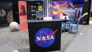 a black bookcase with nasa's blue meatball logo on it sits on a gray carpet on the floor of a comics convention