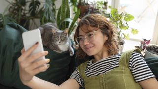 Smiling woman taking selfie with cat on couch at home