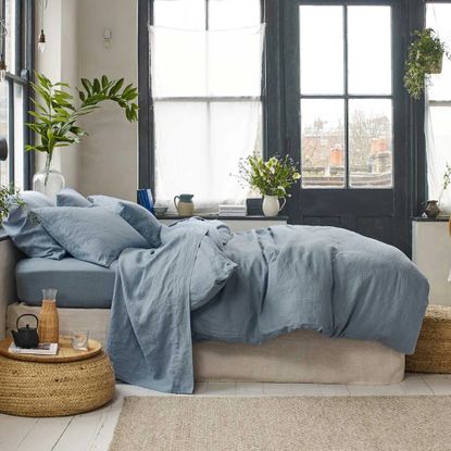 A bedroom with large black-framed windows and a bed dressed with a blue linen duvet cover and pillows