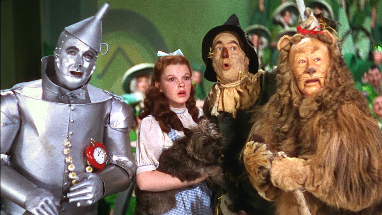 A tin man, a young girl with a little dog, a scarecrow, and a lion posed in a green building