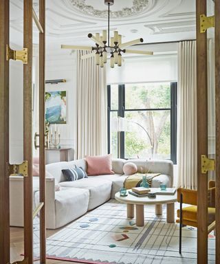neutral living room with off white modular sofa, graphic rug and statement pendant and pops of pink