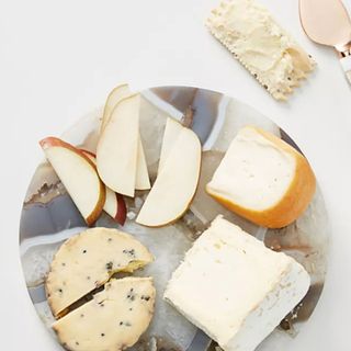 A marbled cheese board pictured on a white background with cheese and a cheese knife. 