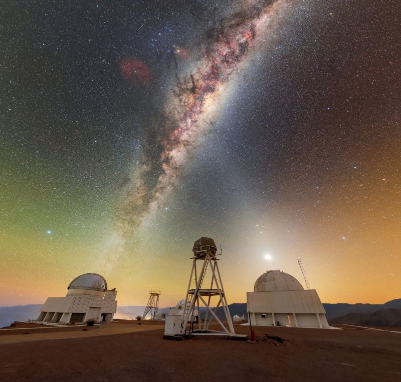 The Milky Way glows in a dark purple and orange night sky over the white domed buildings below.