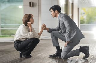 A woman squats as a man rests on one knee and holds her hand, in 'Destined With You.'