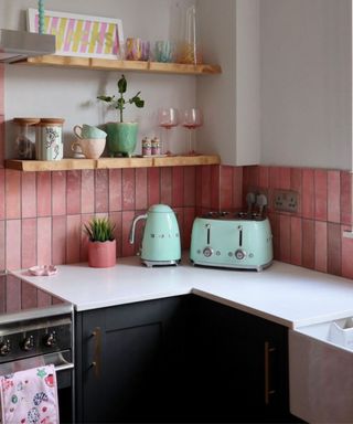 A modern kitchen with pink tiles, wooden shelving and decluttered counter