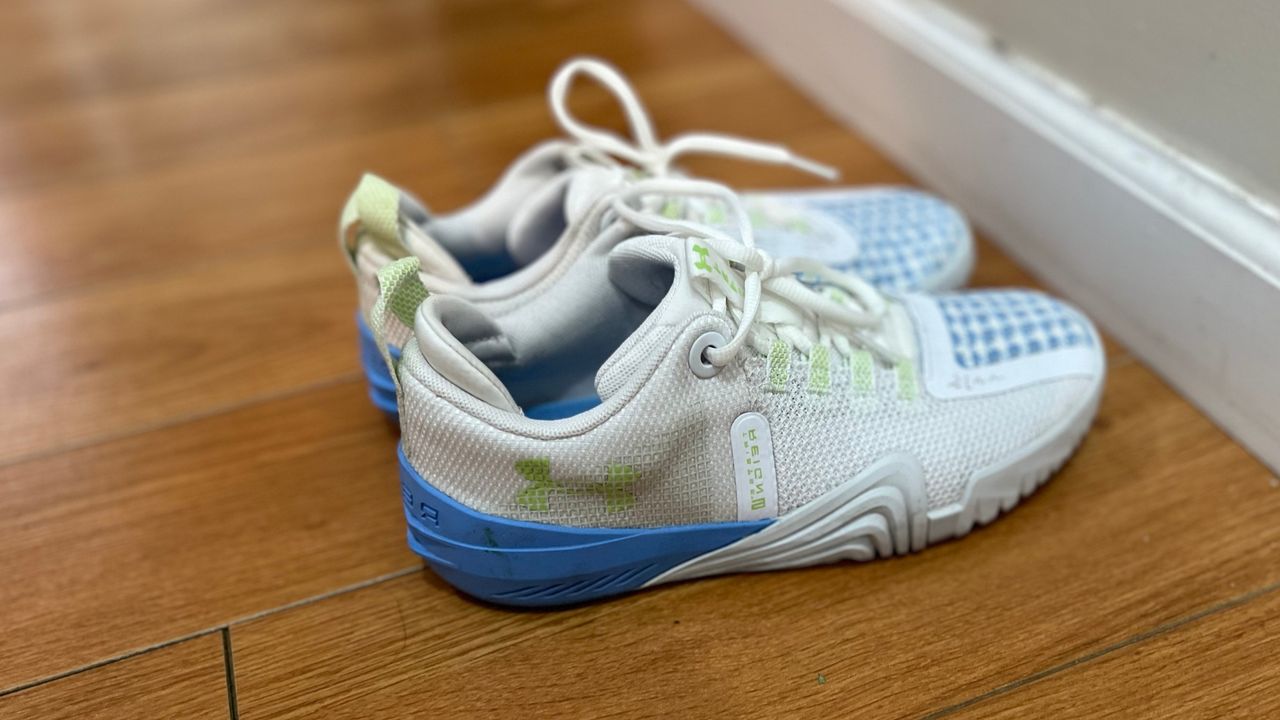 A pair of Under Armour Reign 6 shoes in white on a wooden floor