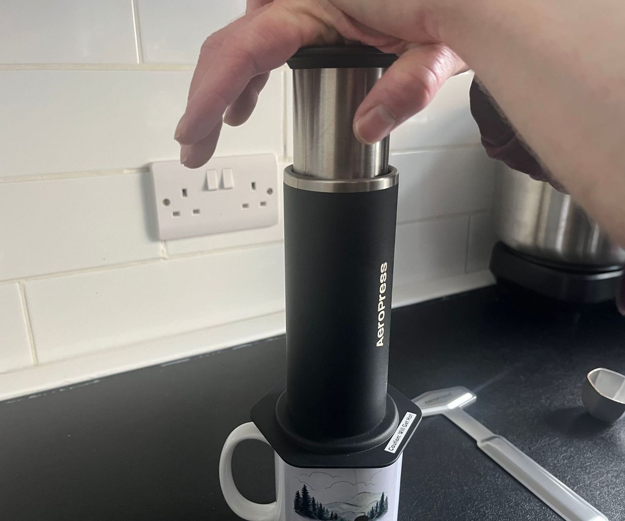 Pressing the stainless steel plunger down in a black AeroPress.