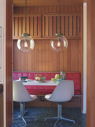 Retro style dining set-up with red leather banquette seating, and white swivel chairs, and glass orb statement lighting.