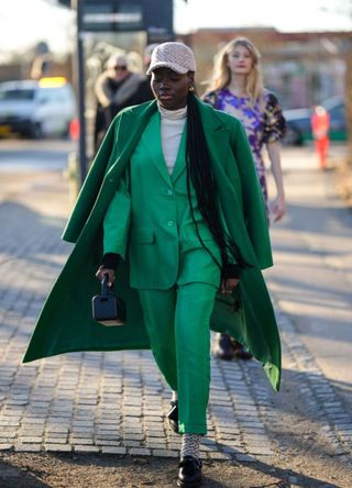 A woman wearing a green suit and trench coat, showing how to layer clothes effectively