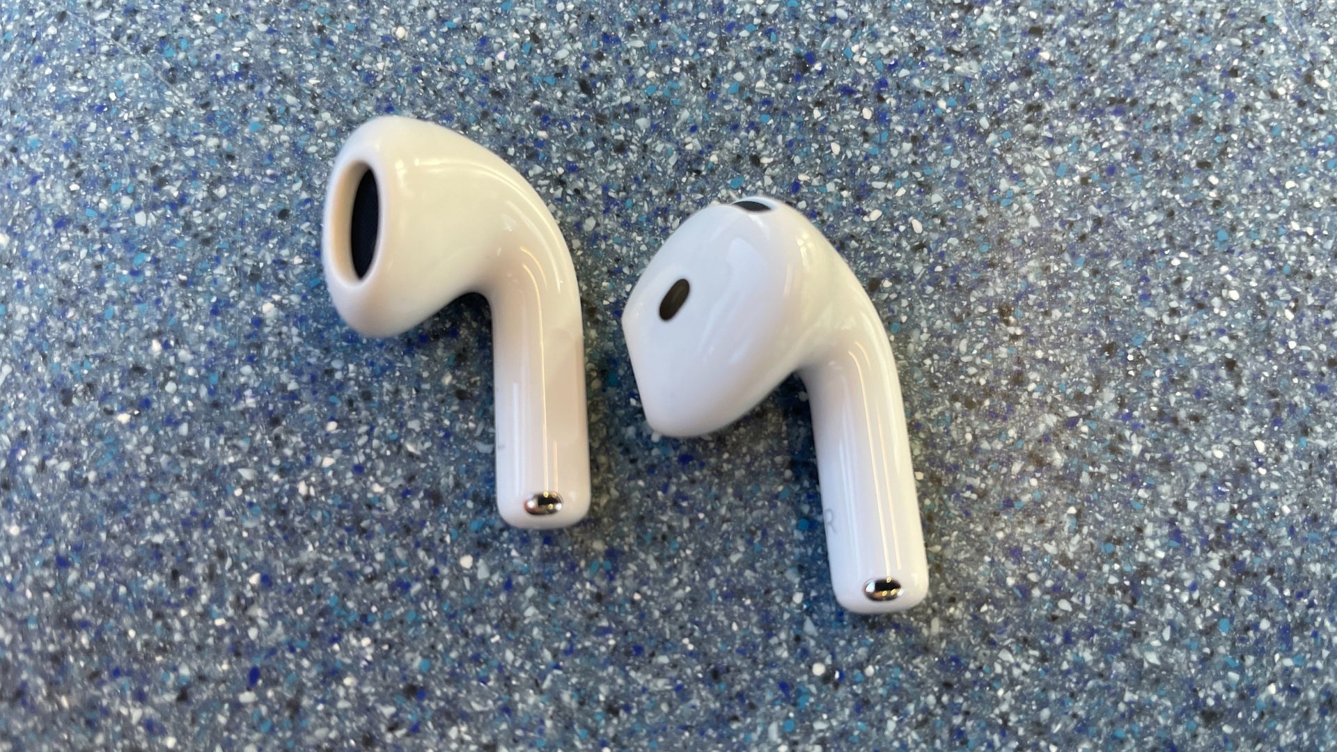 Apple AirPods 5 with Wireless Charging, on a blue table and held in a hand