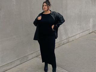 gia wears black dress, black boots, and black jacket while posing outside.