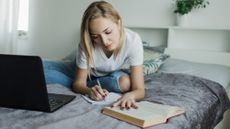 A college student sitting on her bed writing and studying 