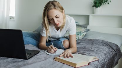 A college student sitting on her bed writing and studying