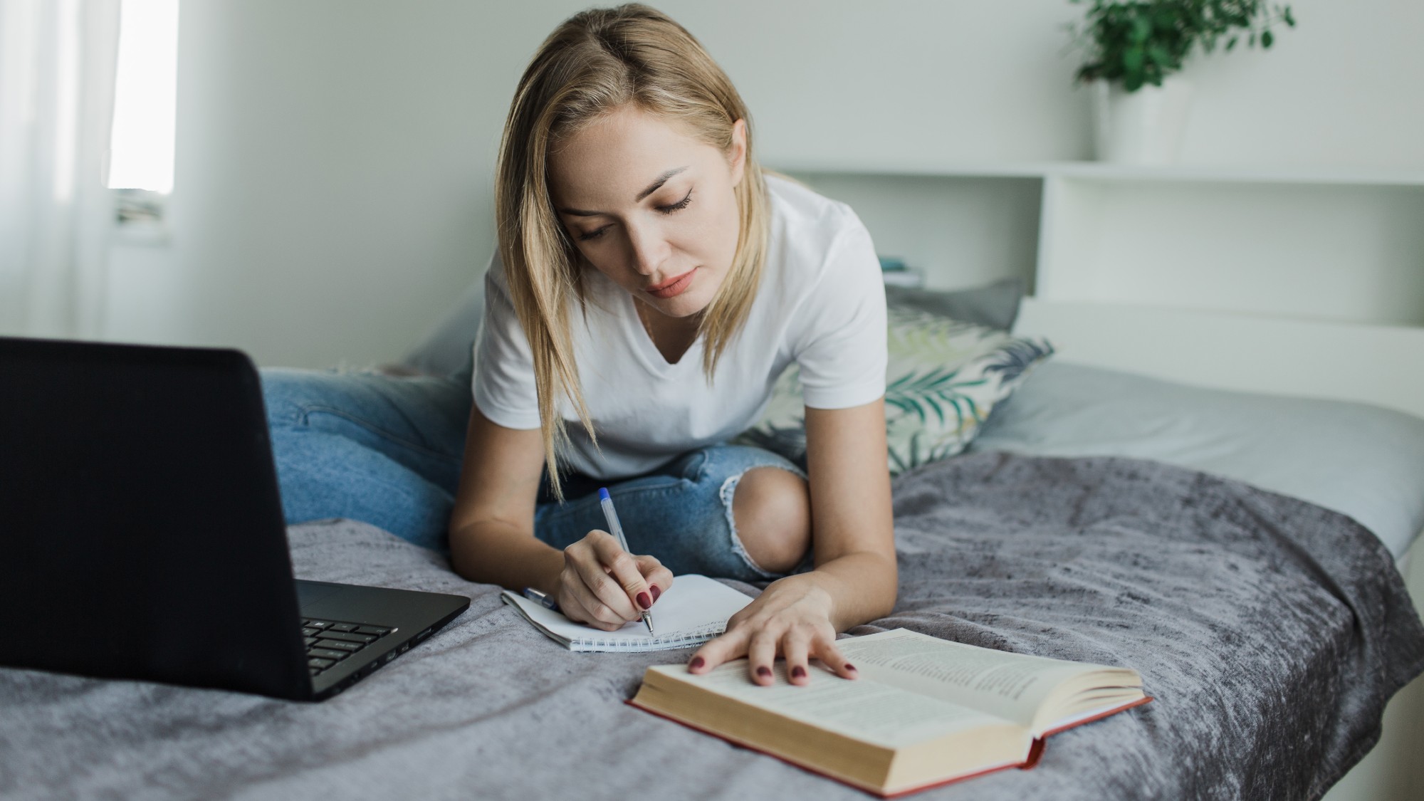 A college student sitting on her bed writing and studying 