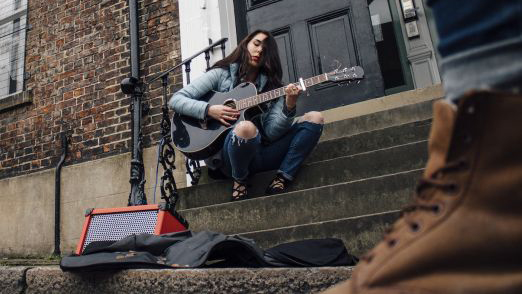 Busker on steps playing acoustic guitar through a Roland Street Cube EX.