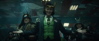 Loki (Tom Hiddleston) stands facing the camera wearing a tattered blue suit, a green waistcoat and a green tie, a smile on his face and his arms outstretched. There is a &quot;LOKI&quot; campaign button on his lapel. Standing behind him are various armed men.