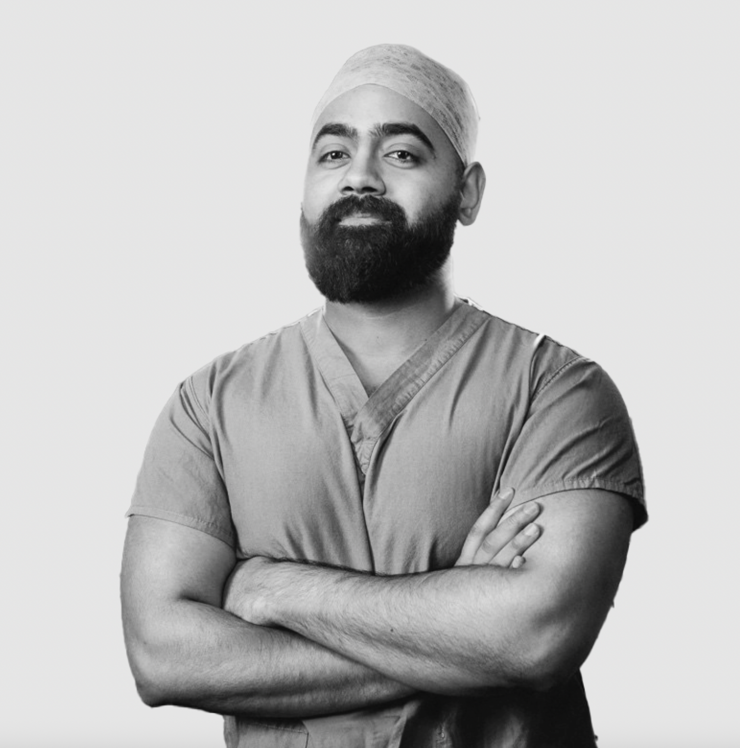 Man stands with his arms crossed, wearing surgical scrubs