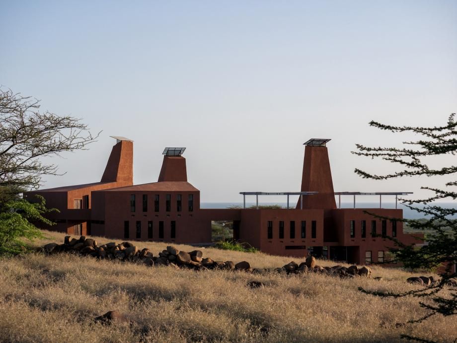 The education campus is surrounded by nature. There are three connected buildings, in burnt brown color. Each building has an element with an opening at the end, that looks like it&#039;s protruding from the building.