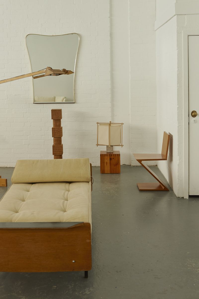 In an industrial gallery, a series of modern furniture items including sofas, sculptural maps, mirrors and wooden chairs create a timeless atmosphere.