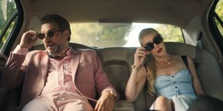 Max (Julian Looman) and Miranda (Elen Rhys) sit in the back of a limousine, dressed in disguise as a wealthy couple. Max is wearing a salmon pink jacket with a matching shirt, trousers and ascot, while Miranda is wearing a strapless sky-blue dress, and both are wearing sunglasses.