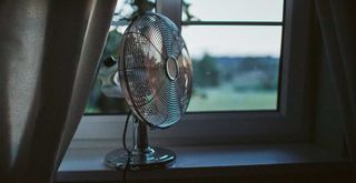 Electric fan sitting just inside an open window to show how to keep a bedroom cool