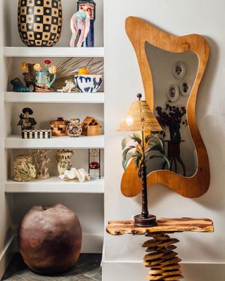 shelves styled with quirky thrift store finds, a unique shaped mirror and table with palm tree lamp