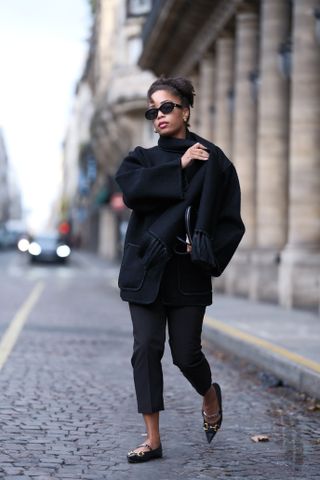 A woman wears an all black outfit with black pointy toe flats in Paris during fashion week.