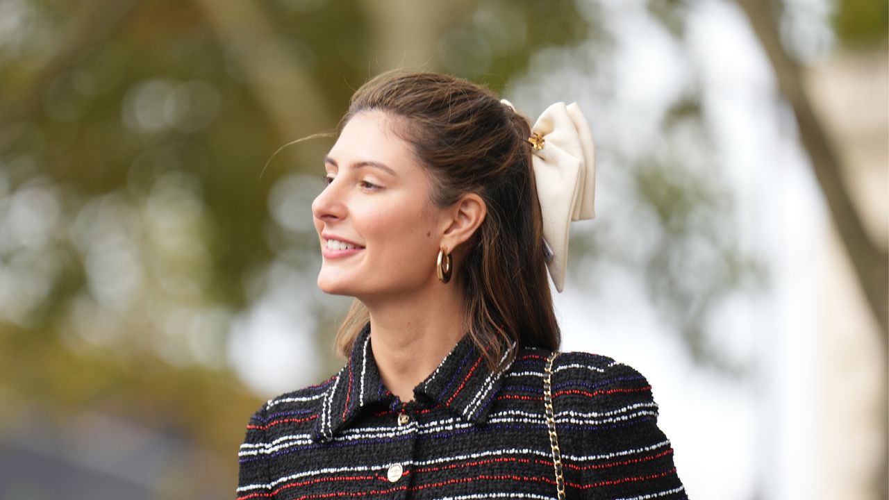 Maria de la Orden wears a bow tie hair bun, golden earrings, a dark blue red and white striped long tweed dress, outside Chanel, during the Womenswear Spring/Summer 2024 as part of Paris Fashion Week on October 03, 2023 in Paris, France