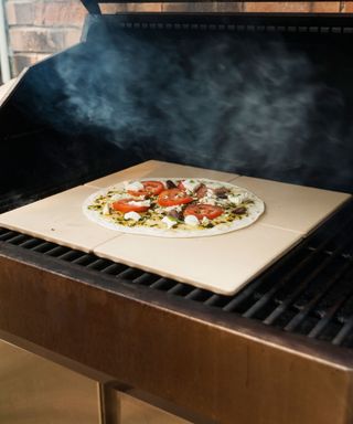 pizza cooking on a pizza stone on a charcoal grill