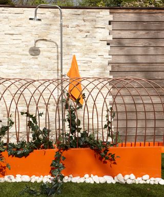 Raised bed garden design featuring a bright orange wall, metal structure and outdoor shower.